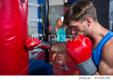 Side view of young male boxer punching red bag Side view of young male boxer punching red bag 34366190