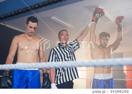 Referee holding hands of winning male boxer by athlete Referee holding hands of winning male boxer by athlete 34366200