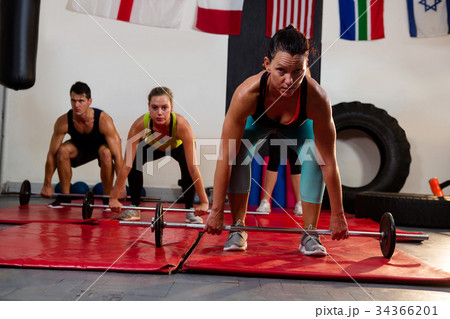 Portrait of female athlete lifting barbell with friends 34366201