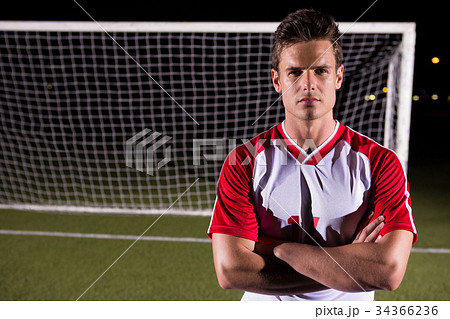 Confident male soccer player standing with arms crossed against goal post on field Confident male soccer player standing with arms crossed against goal post on field 34366236