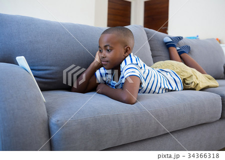 Bored boy looking at mobile phone while lying on gray sofa Bored boy looking at mobile phone while lying on gray sofa 34366318