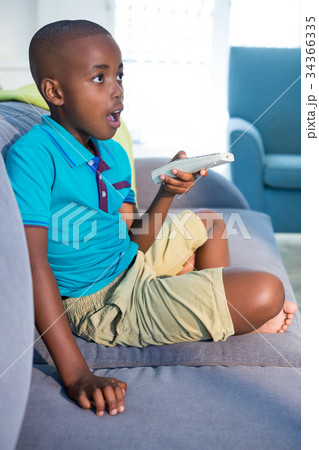 Surprised boy holding remote control while sitting on sofa at home 34366335
