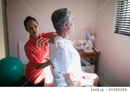 Young female therapist massaging back of senior male patient 34366369