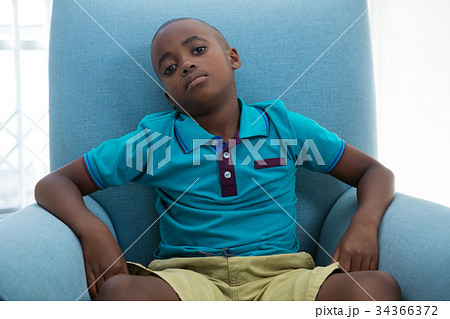 Portrait of boy sitting on blue armchair at home 34366372