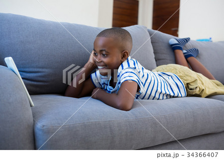 Smiling boy looking at mobile phone while lying on gray sofa Smiling boy looking at mobile phone while lying on gray sofa 34366407