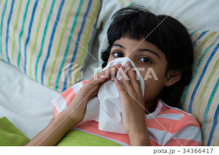 High angle portrait of girl blowing nose on bed High angle portrait of girl blowing nose on bed 34366417