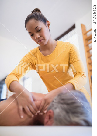 Low angle view of female therapist giving neck massage to male patient Low angle view of female therapist giving neck massage to male patient 34366418
