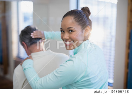 Rear view of portrait of smiling female therapist giving neck massaging to senior male patient Rear view of portrait of smiling female therapist giving neck massaging to senior male patient 34366728