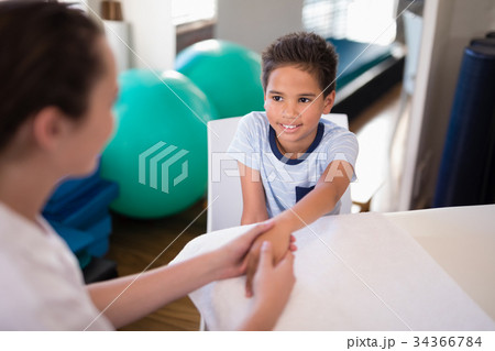 High angle view of smiling boy looking at female therapist examining hand 34366784