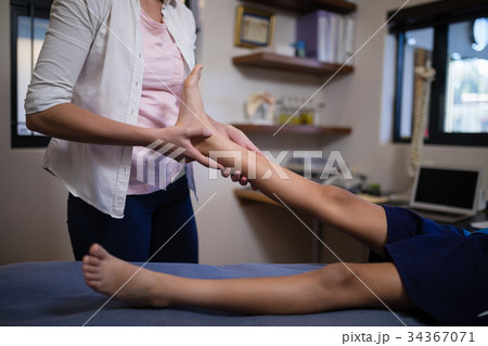 Young female therapist massaging sole of foot with boy on bed 34367071