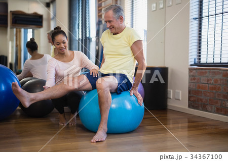 Female therapist helping senior male patient doing leg exercise on blue ball 34367100