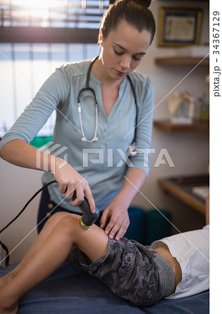 Young female therapist using ultrasound machine on knee of boy Young female therapist using ultrasound machine on knee of boy 34367129