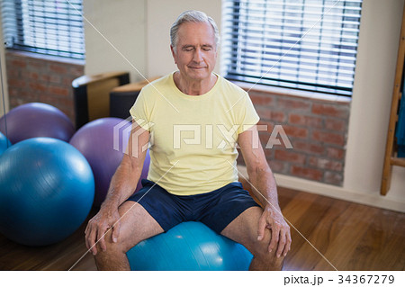 High angle view of senior male patient sitting on exercise ball with eyes closed 34367279