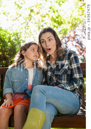 Girl whispering in ears of smiling surprised mother while sitting on bench Girl whispering in ears of smiling surprised mother while sitting on bench 34367479