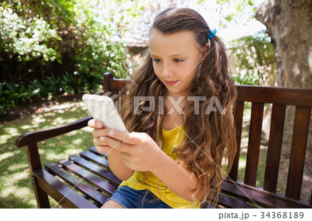 Girl using cellphone while sitting on wooden bench 34368189