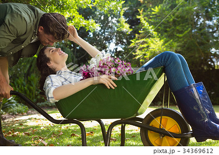 Couple looking face to face while pushing wheelbarrow in garden Couple looking face to face while pushing wheelbarrow in garden 34369612