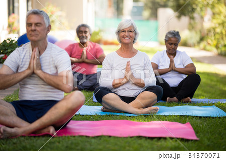 Smiling senior woman meditating in prayer position with friends 34370071