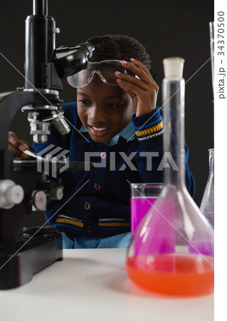 Schoolgirl using microscope against black background Schoolgirl using microscope against black background 34370500