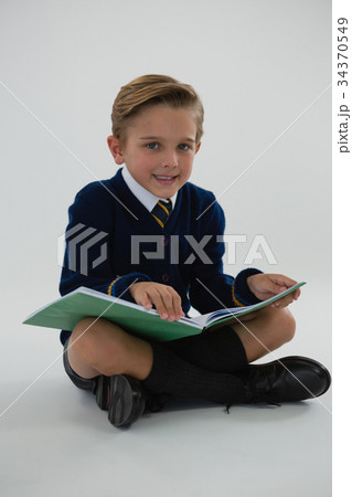 Schoolboy reading book while sitting on white background 34370549