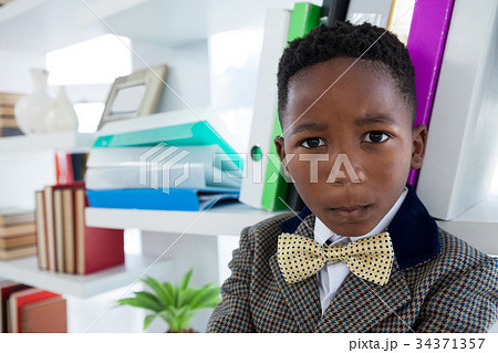 Close up portrait of boy imitating as businessman standing by shelf Close up portrait of boy imitating as businessman standing by shelf 34371357