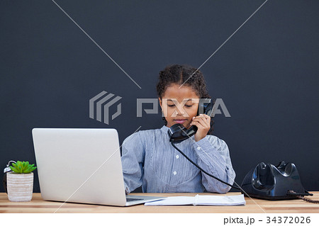 Businesswoman using landline phone while working on laptop 34372026