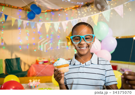 Portrait of cute boy holding cupcake during birthday party Portrait of cute boy holding cupcake during birthday party 34375070