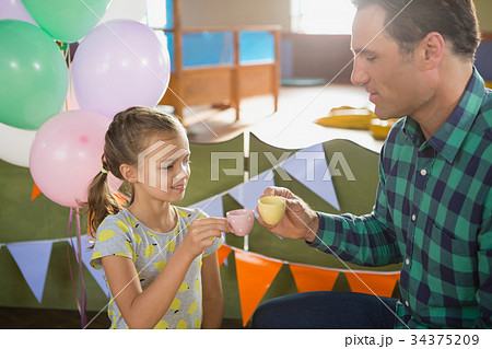 Father and girl toasting their tea cups while playing with toy kitchen set Father and girl toasting their tea cups while playing with toy kitchen set 34375209