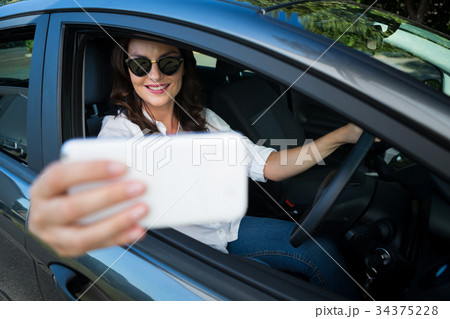 Woman taking selfie with mobile phone in car Woman taking selfie with mobile phone in car 34375228