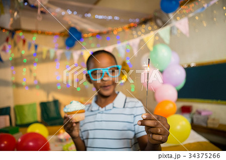 Cute boy holding sparkler and cupcake during birthday party Cute boy holding sparkler and cupcake during birthday party 34375266