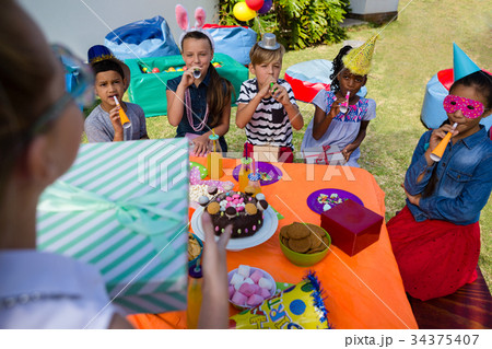 Girl holding gift while friends blowing party horn 34375407