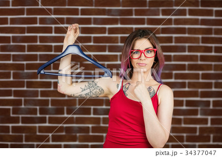 Confused woman holding hanger against brick wall Confused woman holding hanger against brick wall 34377047