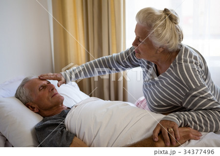 Senior woman sitting by husband sleeping on bed 34377496