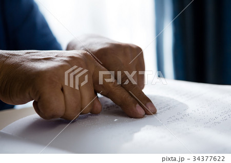 Cropped hands on senior man reading braille book in retirement home Cropped hands on senior man reading braille book in retirement home 34377622