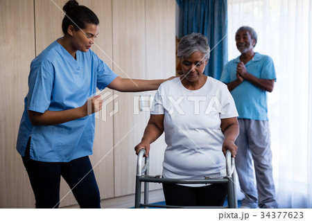 Nurse assisting senior woman in walking with walker Nurse assisting senior woman in walking with walker 34377623
