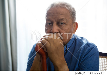 Portrait of sad senior man holding walking cane while sitting on chair 34377712