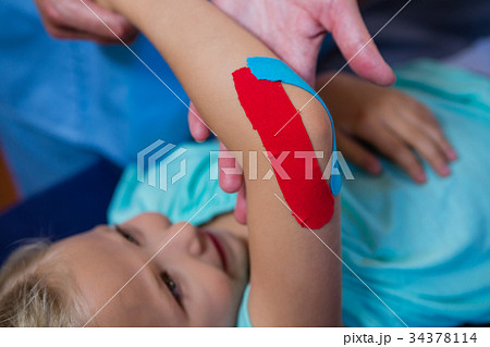 Physiotherapist sticking tape on girl patient Physiotherapist sticking tape on girl patient 34378114