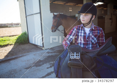 Teenage girl holding horse equipments in the stable 34378297