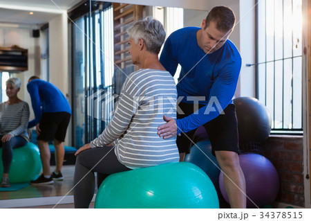 Physiotherapist assisting senior woman on exercise ball 34378515