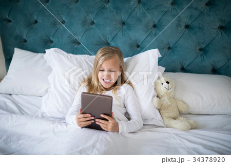 Girl using digital tablet while lying on bed Girl using digital tablet while lying on bed 34378920