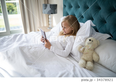 Girl using digital tablet while lying on bed 34378921