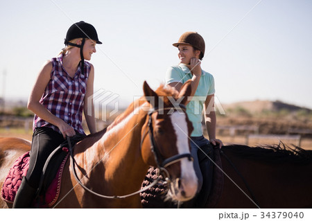 Happy female friends talking while horseback riding 34379040