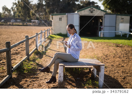 Female vet using digital tablet while sitting at barn 34379162