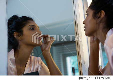 Woman applying makeup reflecting on mirror Woman applying makeup reflecting on mirror 34379186