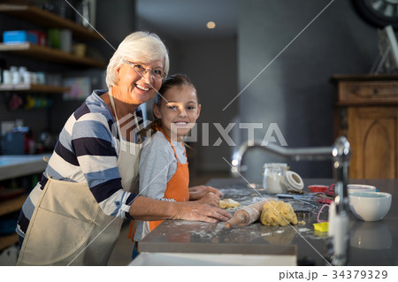 Grandmother and granddaughter posing while flattening dough 34379329