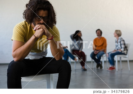 Adult student sitting on chair with friends discussing in background Adult student sitting on chair with friends discussing in background 34379826