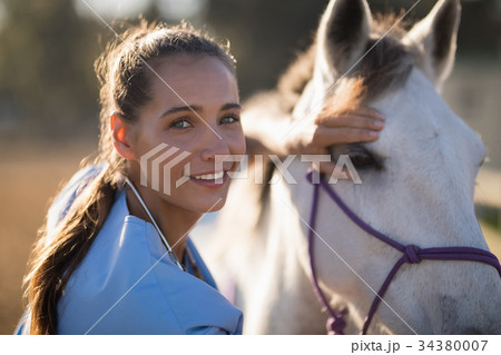 Portrait of smiling female vet checking horse Portrait of smiling female vet checking horse 34380007