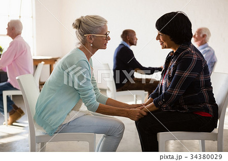 Side view of senior friends holding hands while siting on chair Side view of senior friends holding hands while siting on chair 34380029