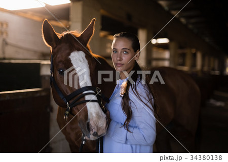 Confident female vet standing by horse in stable Confident female vet standing by horse in stable 34380138