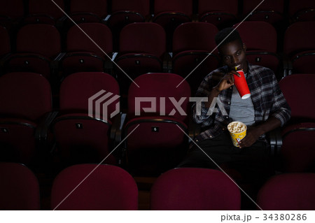 Man having cold drink while watching movie Man having cold drink while watching movie 34380286