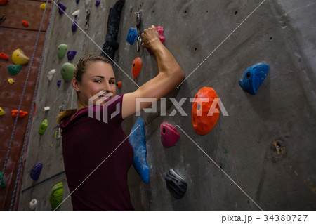 Portrait of confident female athlete climbing wall in gym 34380727